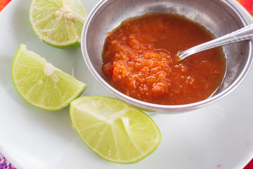 Chili sauce served on a metal bowl with lime slices