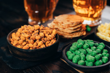 Appetizing beer snacks close up. Crunchy salty nuts, crackers and corn with two mugs of lager. Oktoberfest food, pub concept