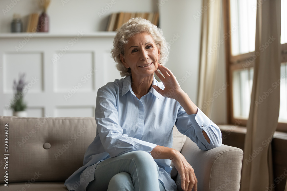 Wall mural portrait of happy mature 60s grandmother sit on couch in living room look at camera posing, smiling 