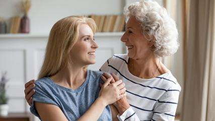 Smiling senior 60s mother and adult millennial daughter hug embrace enjoy family home weekend together, happy loving mature mom and grownup girl child cuddle, having close tender moment