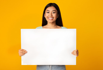 Asian Woman Holding Empty White Poster Standing On Yellow Background