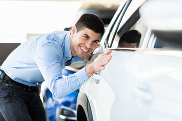 Happy Guy Touching His Auto In Dealership Showroom