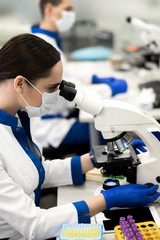 Researcher in medical mask using microscope in laboratory