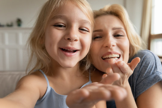 Cute little preschooler girl and young mother have fun make self-portrait picture on camera together, overjoyed mom and small daughter smile laugh take selfie, play enjoy family weekend at home