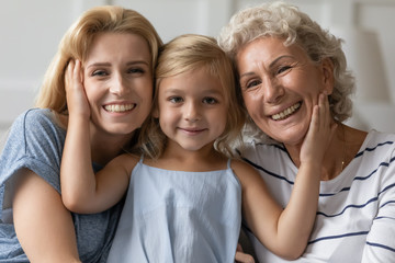 Portrait of cute little preschooler girl hug cuddle with happy young mother and mature grandmother...