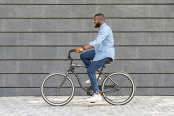 Way to office. Young african american businessman riding bicycle to work