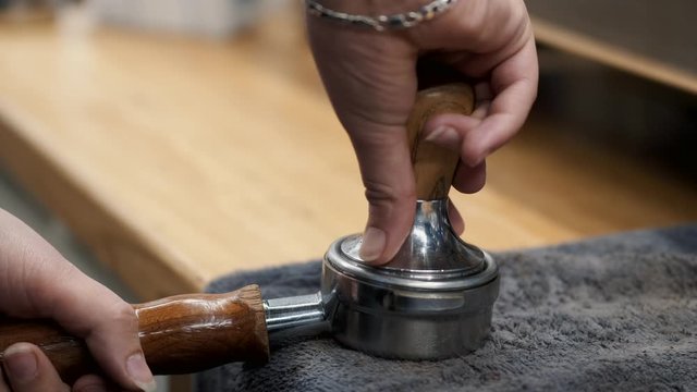 A barista is tamping grounded beans of coffee.The coffee lover is making a latte.
