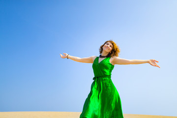 Fototapeta na wymiar 緑のドレスを着て砂丘に立つ白人女性