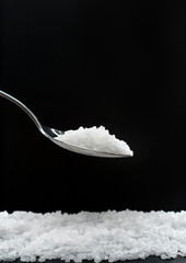 coarse sea salt in a spoon on a black background with copy space