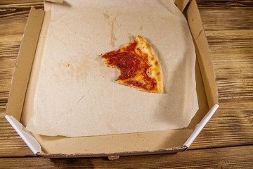 Bitten slice of pizza in cardboard box on a wooden table. Concept for home delivery of food, fast food, delivery of pizza