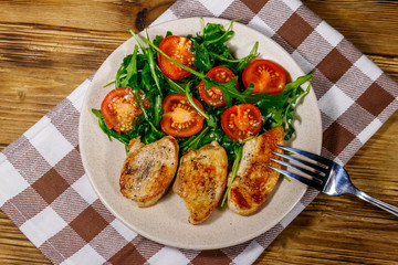 Fried chicken breast with salad of fresh arugula and cherry tomatoes on wooden table. Top view