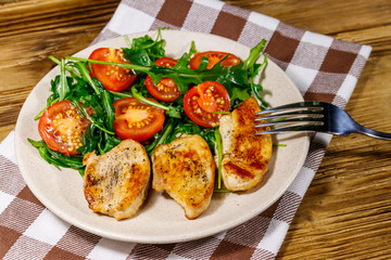 Fried chicken breast with salad of fresh arugula and cherry tomatoes on wooden table