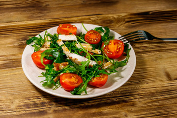 Tasty salad of fried chicken breast, fresh arugula and cherry tomatoes on wooden table
