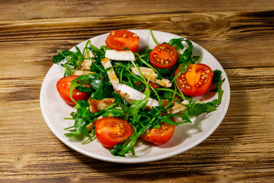 Tasty salad of fried chicken breast, fresh arugula and cherry tomatoes on wooden table