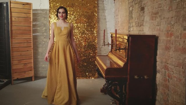 Girl with finger wave hairstyle in gold elegant dress goes spinning piano on backdrop shine sparkle glitter screen. Holiday stylized New Year in style Retro Great Gatsby women Vogue fashion old 1920