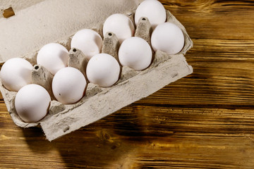 Raw chicken eggs in cardboard egg box on wooden table. Top view