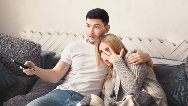 Terrified Young Couple Watching Scary Movie At Home