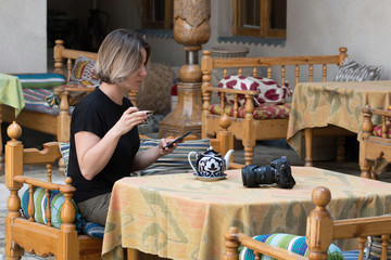 European tourist (young woman) drinks tea at the table with teapot, cup (piala) and photo camera. Uzbekistan, Central Asia.