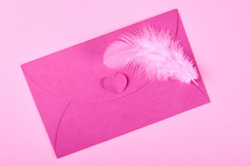 Envelope and feather on pink background composition.