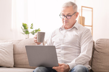 Elderly Man Looking At Laptop And Having Coffee