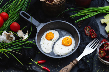 Table top scene with raw vegan eggs made of coconut butter and cashew in a dark frying pan with chilli pepper, dried tomato and organic garlic. Raw food for vegan menu.