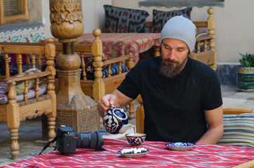 A tourist (man) pouring tea from tea pot in the cup in traditional uzbek interior. Bukhara, Uzbekistan, Central Asia.