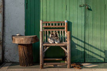 White canvas shoes put on a wooden chair to dry it at the front of the green wooden house door.