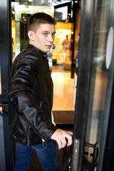 Street fashion. Glamor young man in black Leather Jacket at the city street. Stylish man go to clothing store. Fashion boutique.