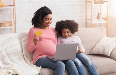 Pregnant Mom With Laptop And Credit Card Shopping Online With Daughter