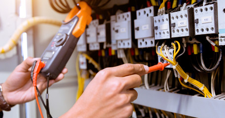 Electrician measurements with multimeter testing current electric in control panel.