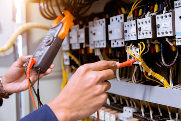 Electrician measurements with multimeter testing current electric in control panel.