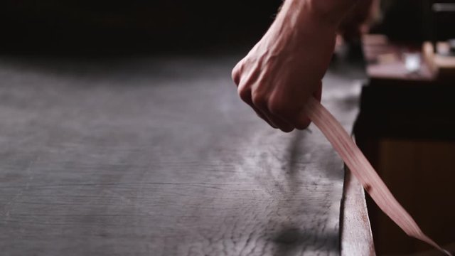 A leather master is measuring material with a tape measure. The tanner is making hand-made leather men&rsquo;s belt.