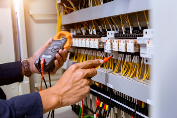 Electrician measurements with multimeter testing current electric in control panel.