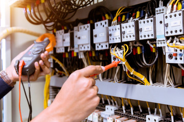 Electrician measurements with multimeter testing current electric in control panel.