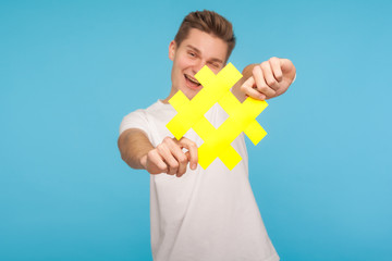 Follow trendy blog. Happy cheerful man in t-shirt holding out yellow hashtag symbol to camera,...