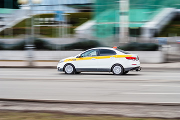 Fototapeta na wymiar Motion city street scene with white taxi vehicle. Fast moving white taxi car on Moscow streets