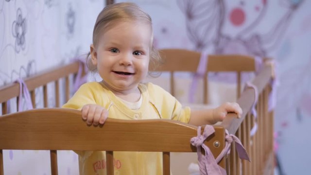Little baby is standing in bed. Little girl smiling in bed.