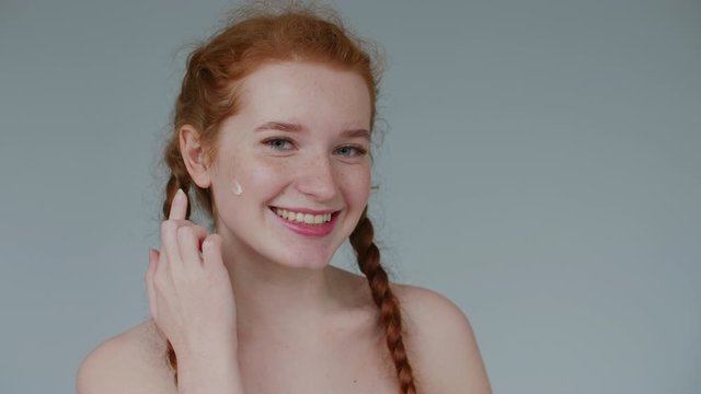 Happy young girl using cream. Natural beauty, face skin care, cosmetic advertising concept. Close up portrait. Copy, empty space for text
