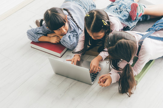 Three aisan children, Three sister, lay on the floor and use a laptop to do their schoolwork.
