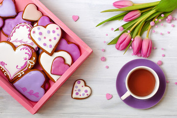 Gingerbread cookies, tea and a bouquet of tulips. Festive composition with homemade heart-shaped cookies and tulips.