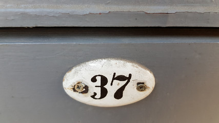 Retro style white nameplate with black figures of three and seven. Number closeup on old door panel painted in grey color. Architectural details.