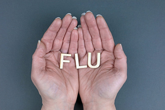 Hands Holding Wooden Letters Spelling The Word Flu. Carrying The Influenza Virus Concept.