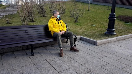 Sick man take on medical mask sitting on a park bench