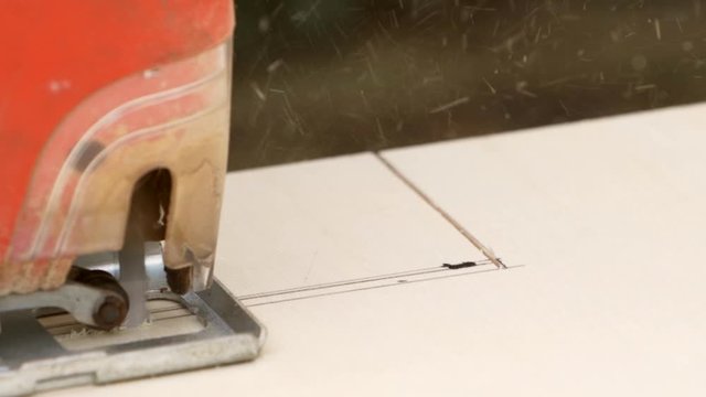 Electric jigsaw in slow motion, sawing from left to right in a multiplex pine  board.
