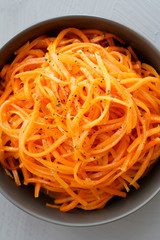 Macro shot of spicy orean carrot salad with oil, garlic and black pepper in grey bowl. Grey table, high resolution