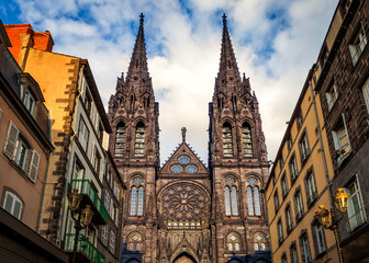 Beautiful, impressive cathedral of Clermont Ferrand in France, made from dark volcanic rocks lighten by golden sunset sun light and old, traditional French buildings