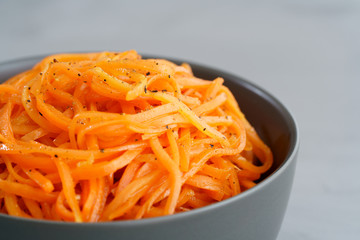 Macro shot of spicy orean carrot salad with oil, garlic and black pepper in grey bowl. Grey table, high resolution