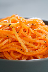 Macro shot of spicy orean carrot salad with oil, garlic and black pepper in grey bowl. Grey table, high resolution