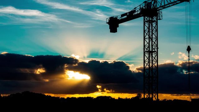 Beautiful Sunset with sun rays over the city with a crane silhouette, timelaps 