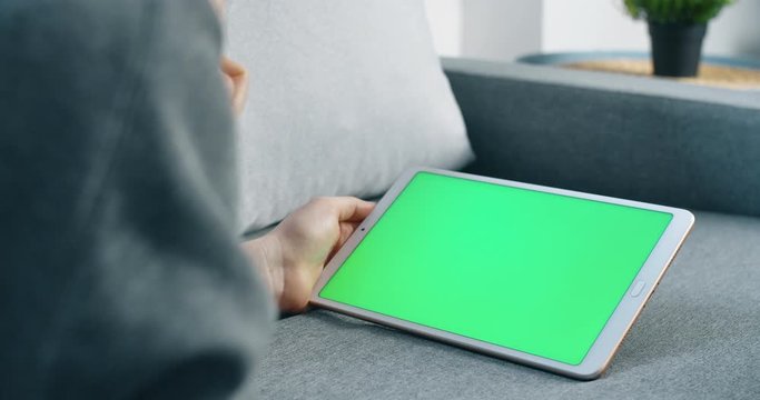 Young womans hand holding tablet with green screen on sofa. Woman on couch using tablet for shopping or watching video. Close up lifestyle concept. 4K.